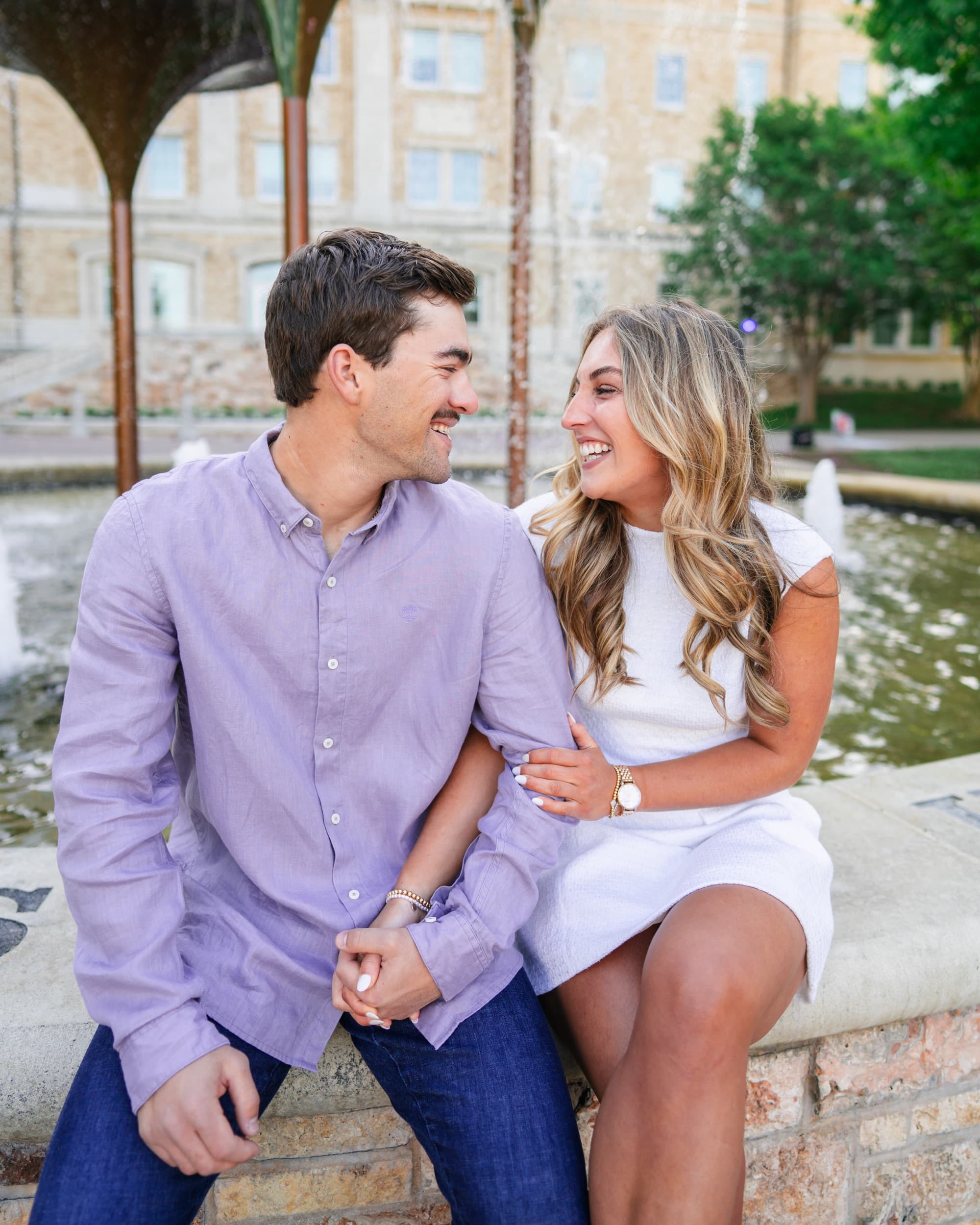 Couple laughing together arm in arm on a fountain ledge, sharing a joyful moment.
